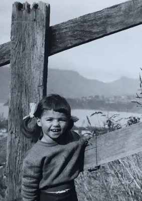 Old black and white photo of a small child smiling beside a wooden fence post